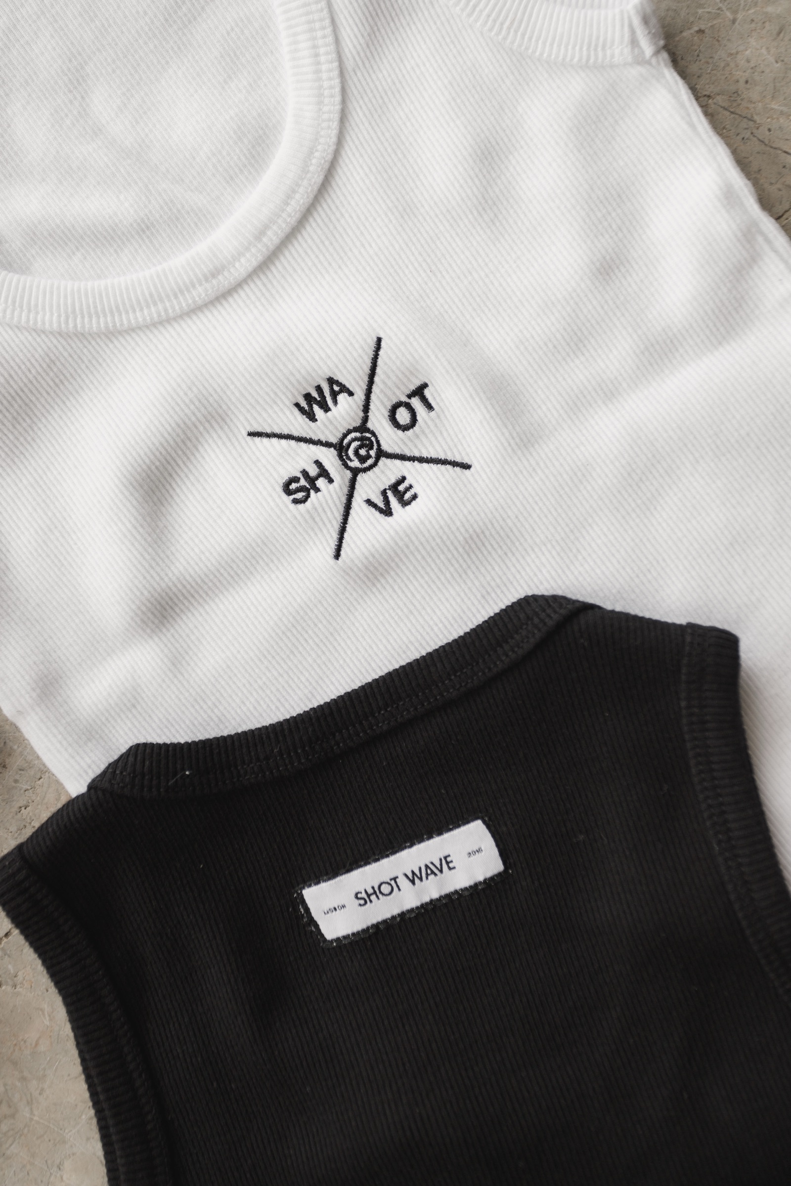 White and black ribbed tank tops with Shot Wave compass-style embroidered logo on the chest