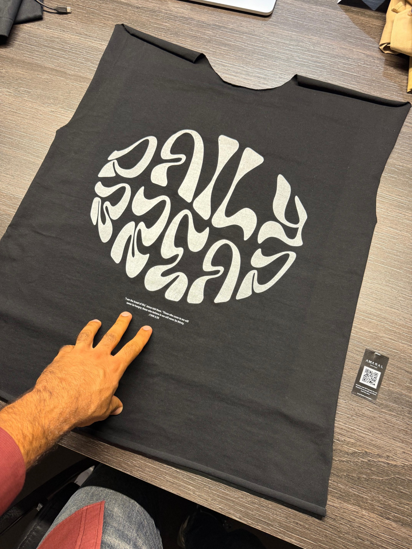 Dark grey t-shirt panel with large white circular abstract typographic graphic being inspected on work table