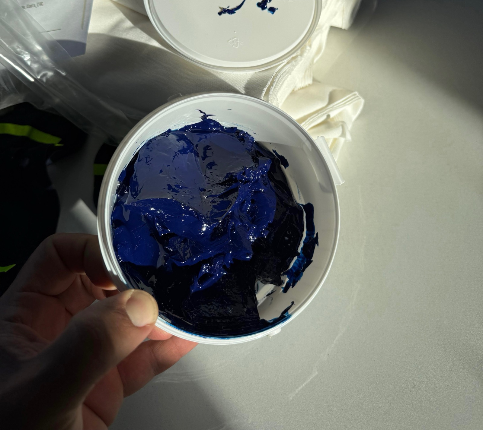 Hand holding container of dark navy blue screen-printing ink ready for garment printing process