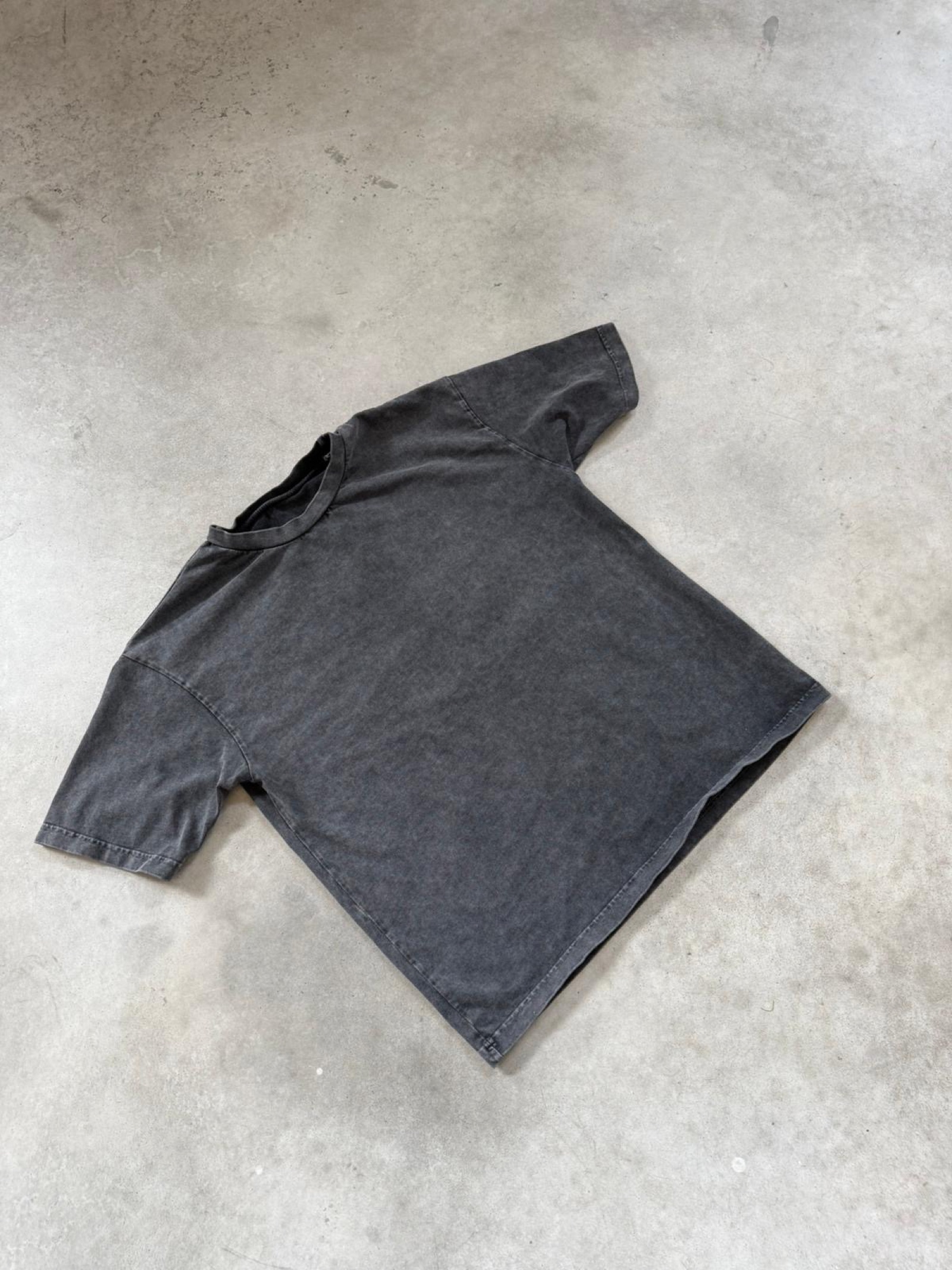 Charcoal acid-washed oversized t-shirt laid flat showing relaxed boxy silhouette and washed-out finish
