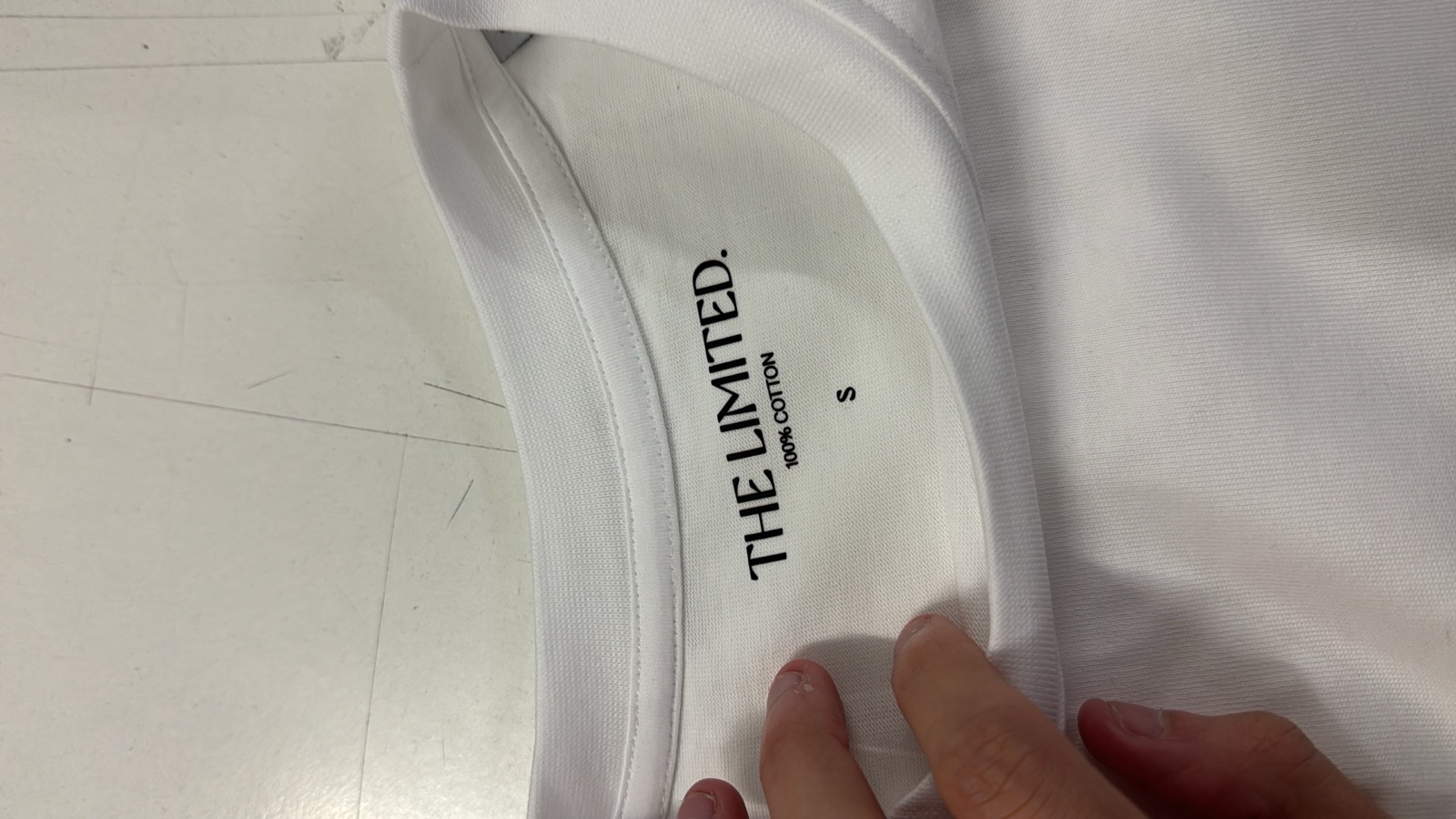 Interior neck print of white t-shirt reading THE LIMITED 100% COTTON showing direct-to-garment printed label