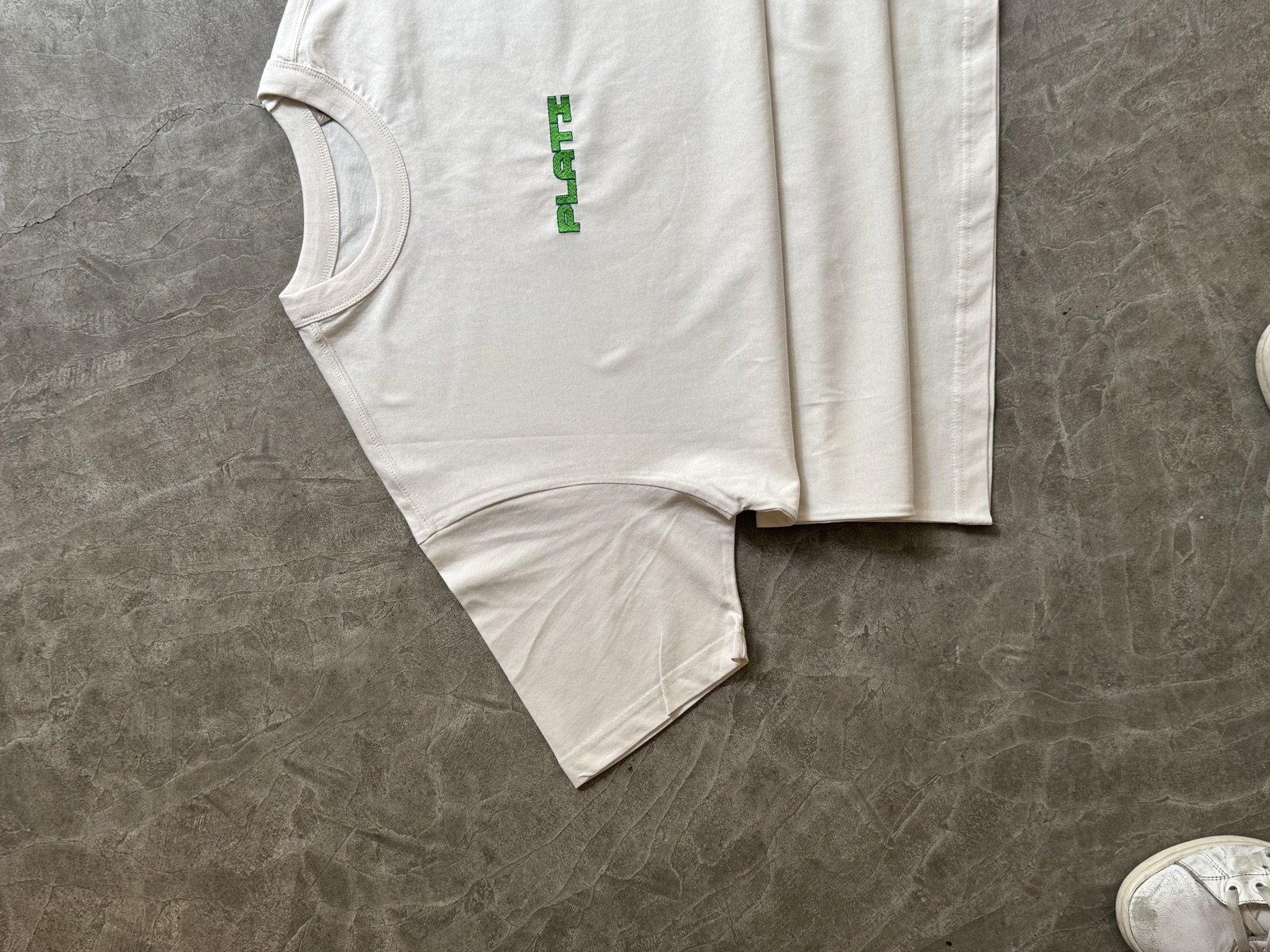 Corner detail of cream oversized t-shirt with partial red script text showing cross-stitched interior hem