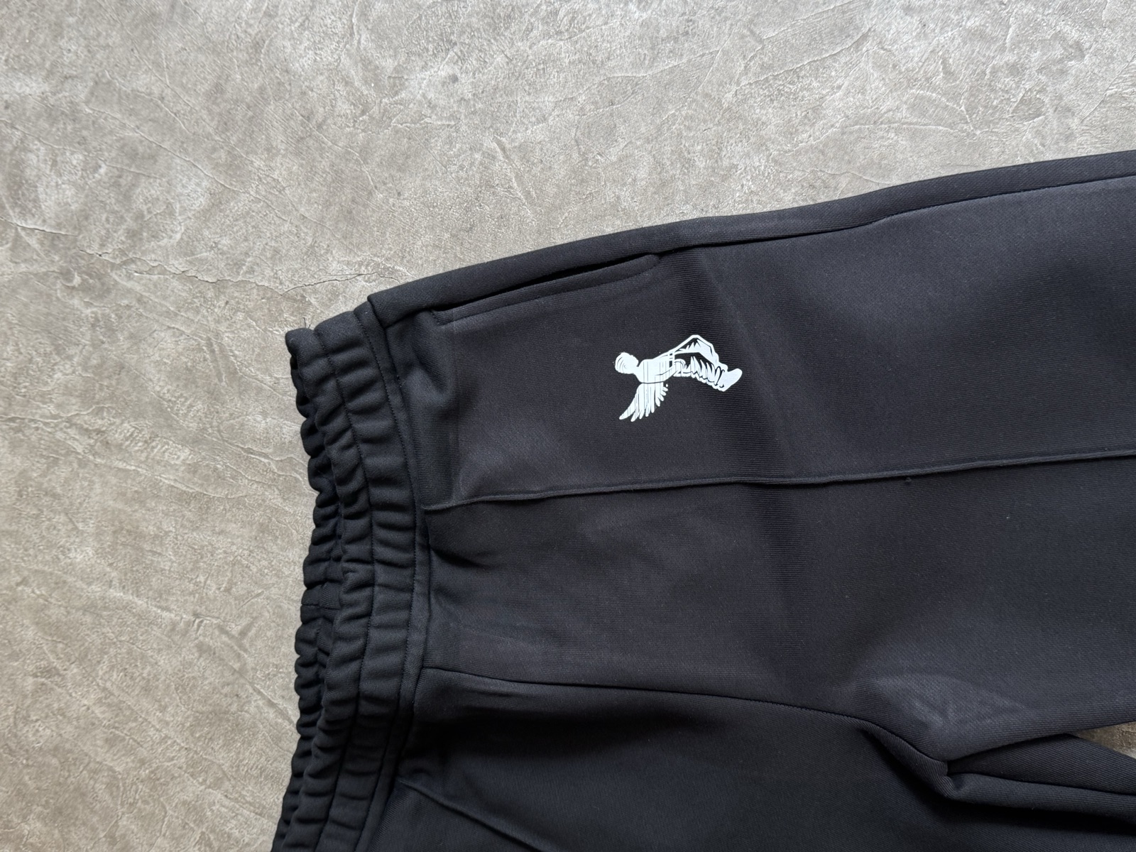 White oversized t-shirt with small green chest logo laid on concrete surface showing drop-shoulder silhouette