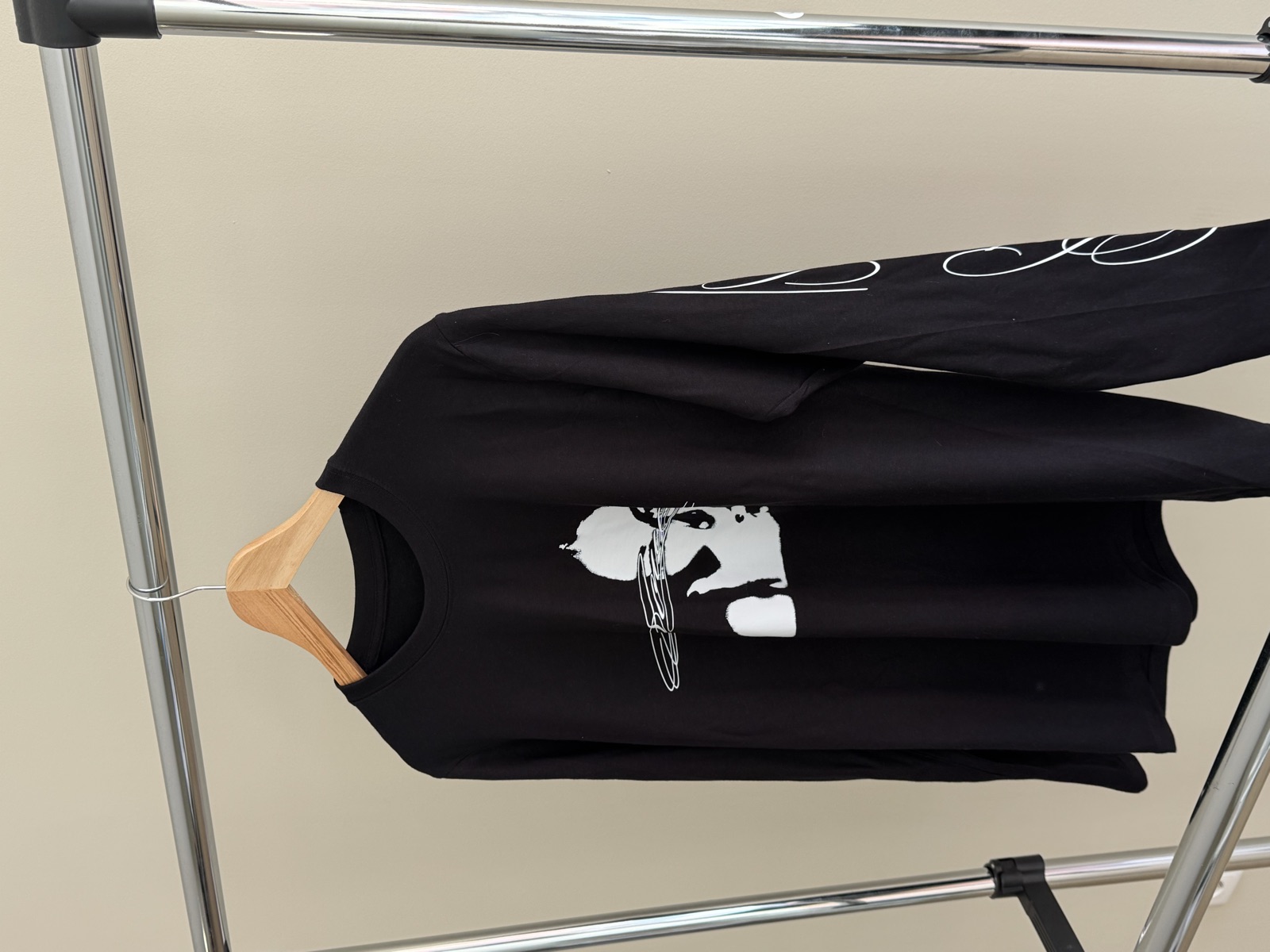 Black long-sleeve t-shirt on wooden hanger featuring white artistic face portrait print and sleeve script text