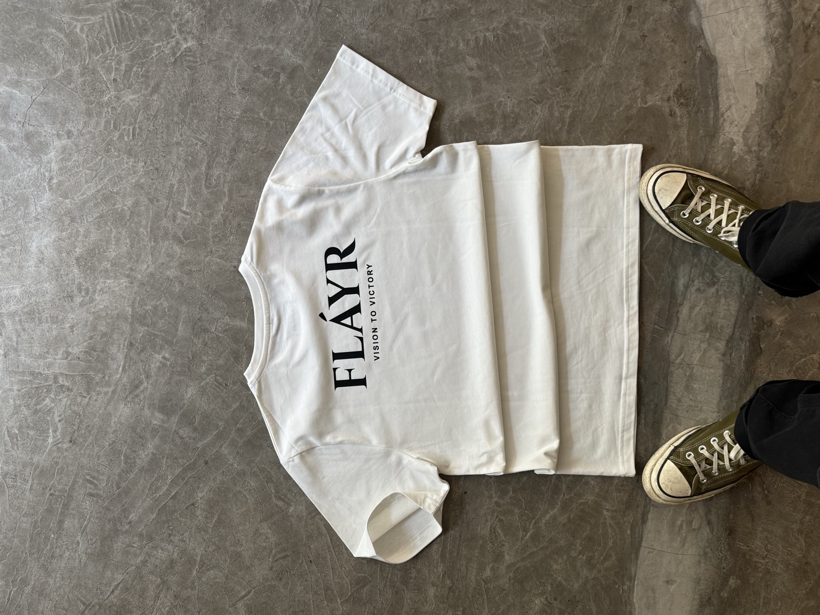 White oversized t-shirt laid flat printed with FLAYR brand name in black serif lettering on the chest