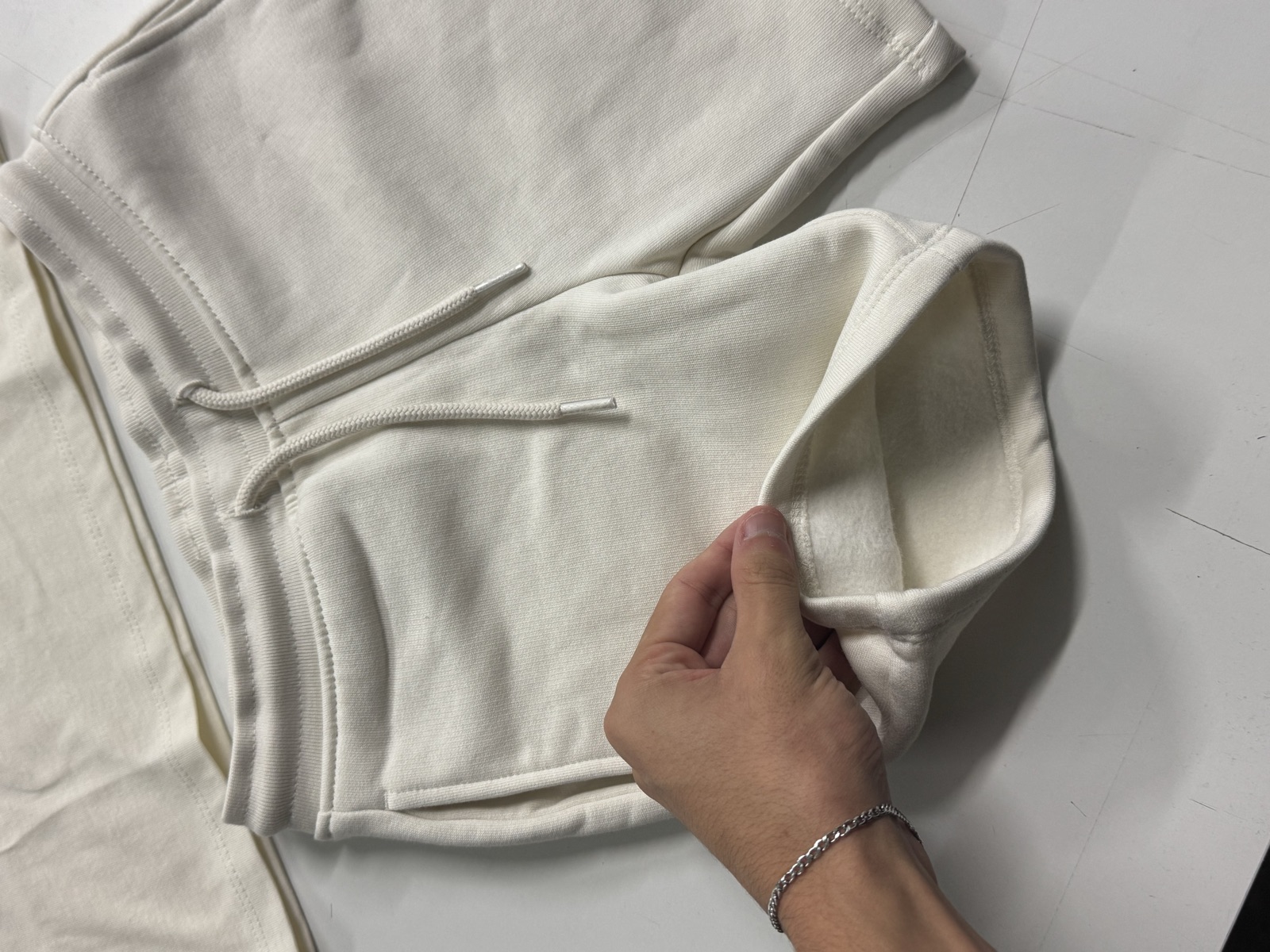 Off-white fleece-lined hoodie laid flat with hand lifting fabric to reveal soft brushed fleece interior
