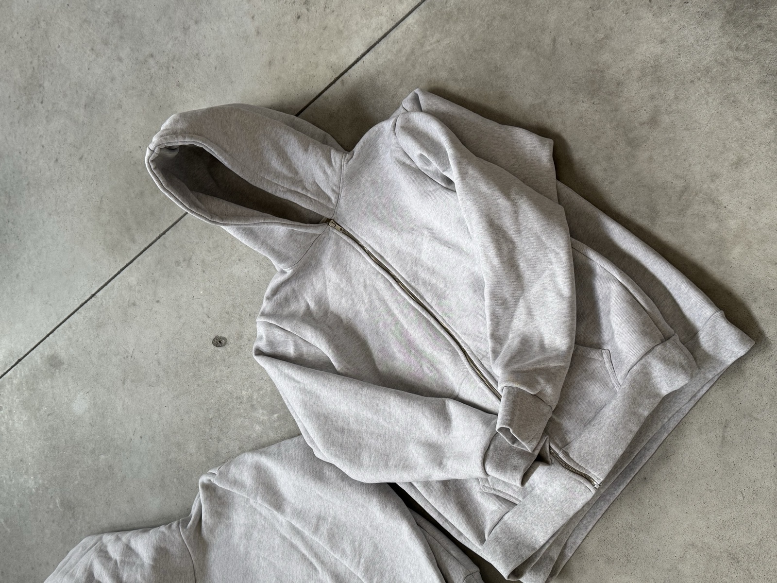 Grey heather pullover hoodie folded on concrete floor showing hood kangaroo pocket and relaxed boxy silhouette