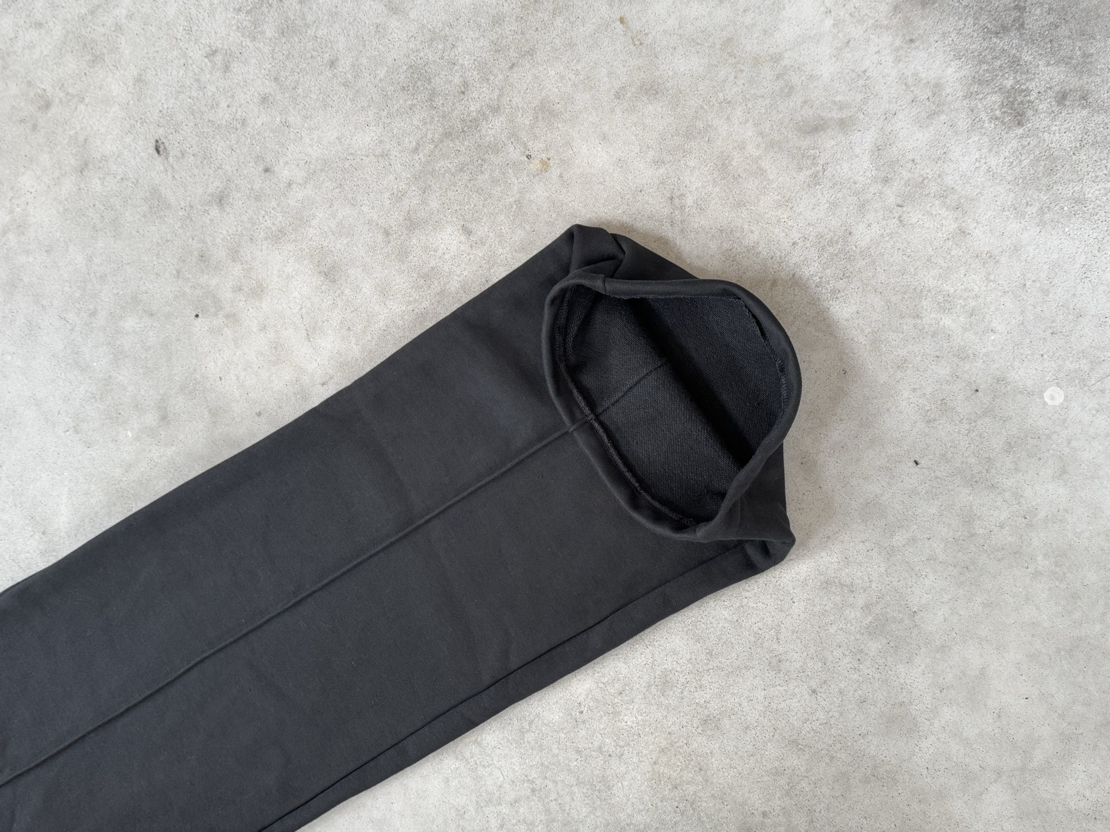 Black woven trousers leg folded to display hemline and slim tapered cut on concrete floor