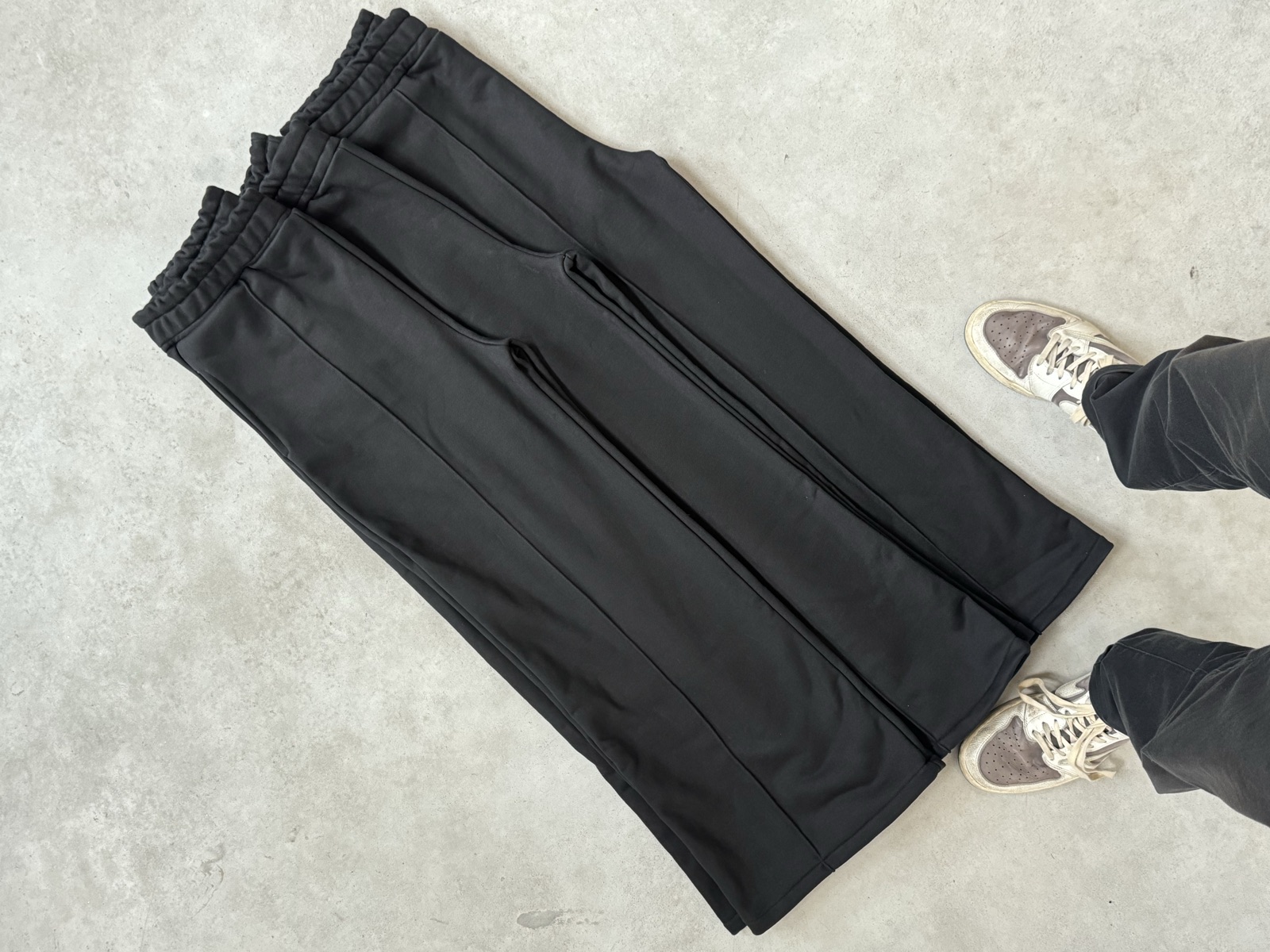 Full-length black tailored jogger trousers with elasticated waist centre crease and wide-leg silhouette