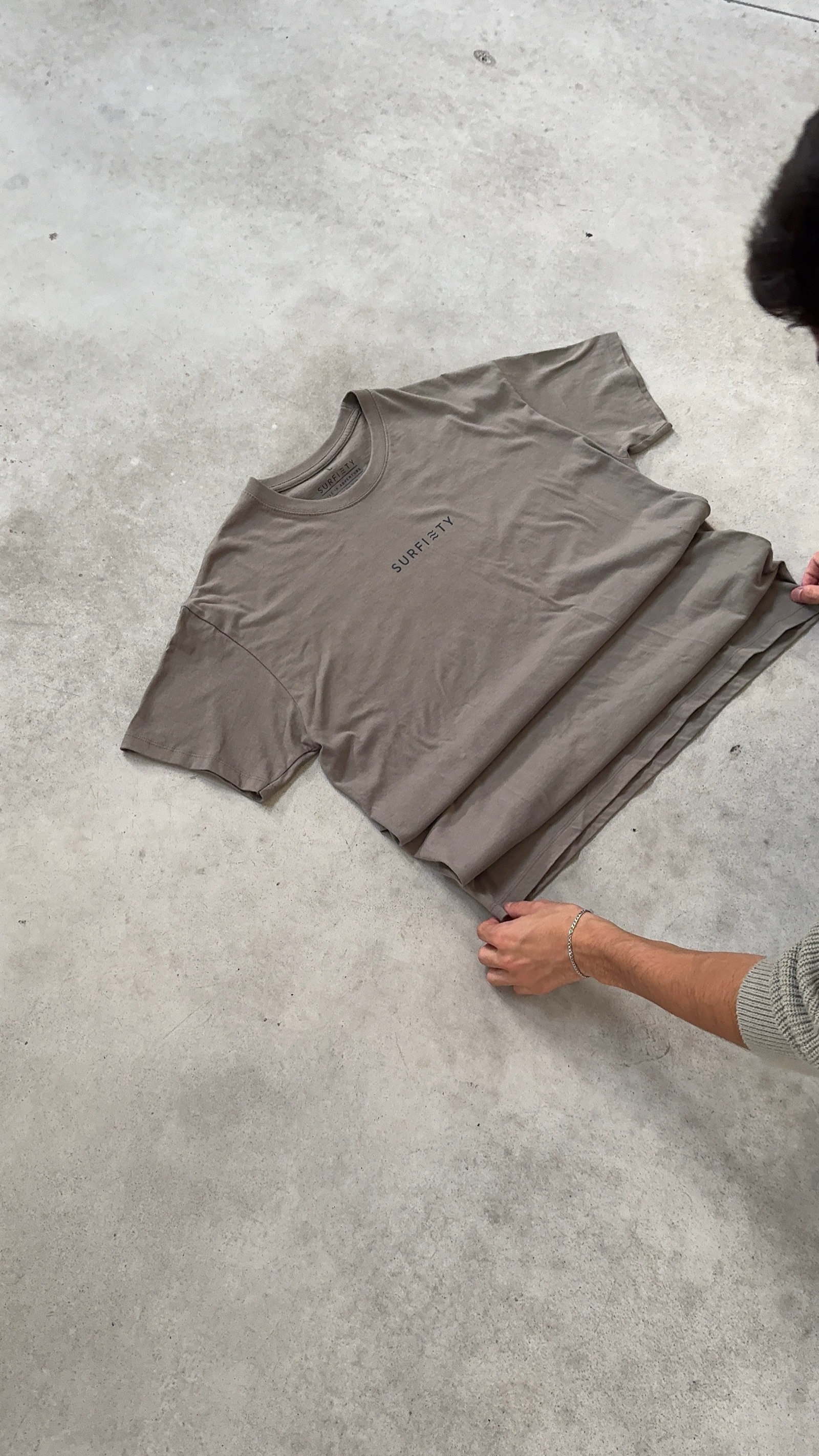 Olive-toned oversized t-shirt showing small centred Surfiety chest text and relaxed drop-shoulder cut