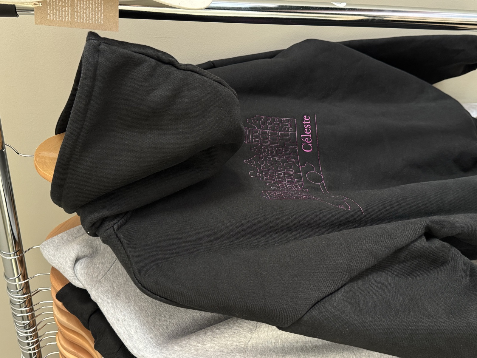 Washed black hoodie with pink line-art graphic and Celeste text printed on the chest hanging on chrome rack