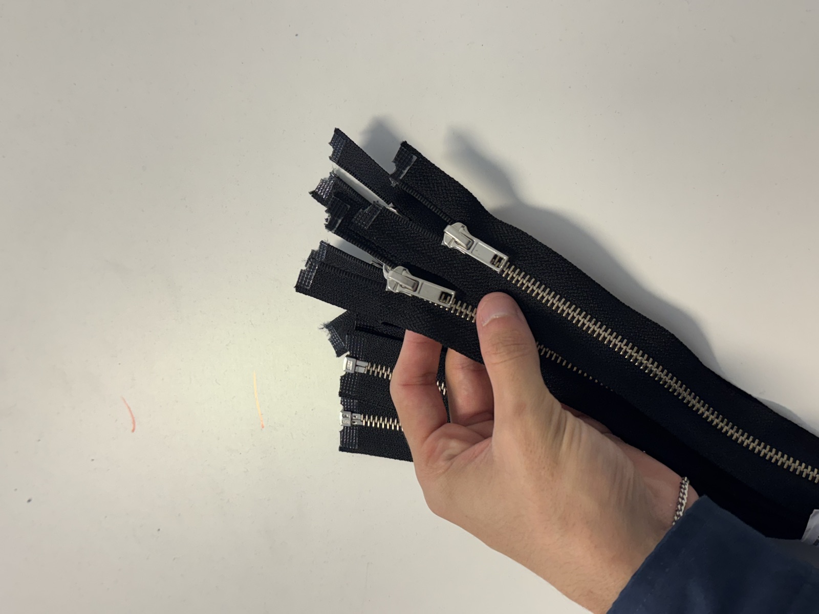 Hand holding bundle of black metal zippers with silver teeth and pulls ready for garment production