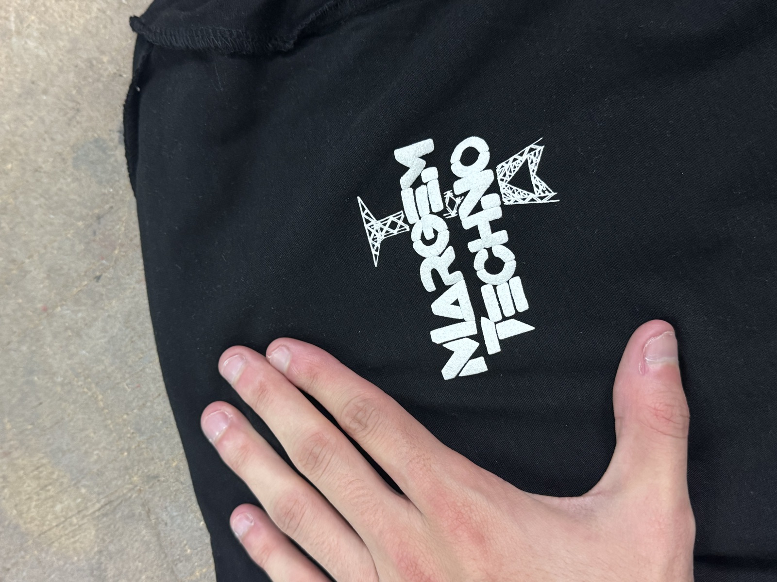 Close-up of black garment with white Margem Techno screen-printed graphic featuring geometric arrow design