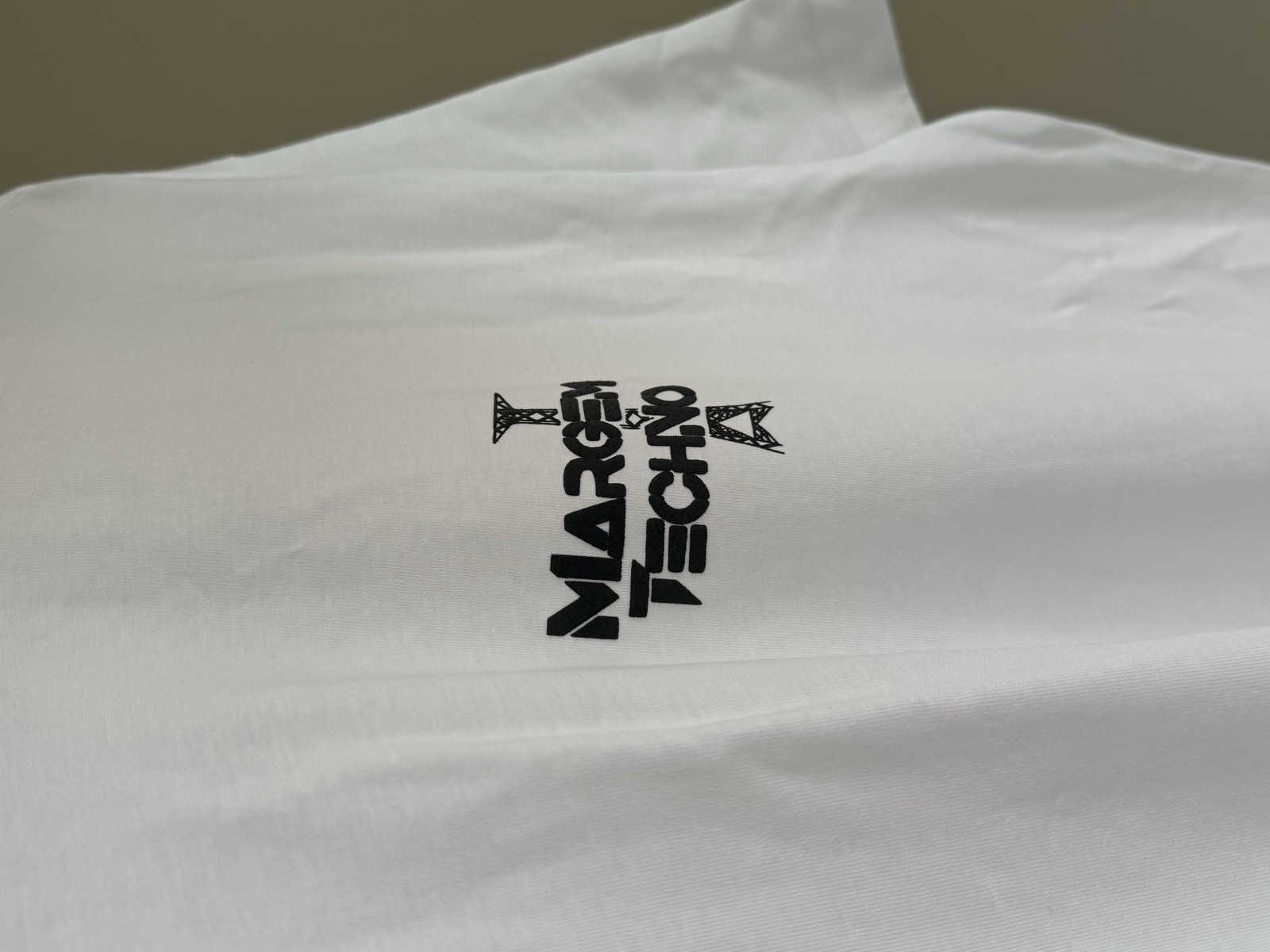 White t-shirt with black Margem Techno logo print featuring geometric arrow motif on the chest