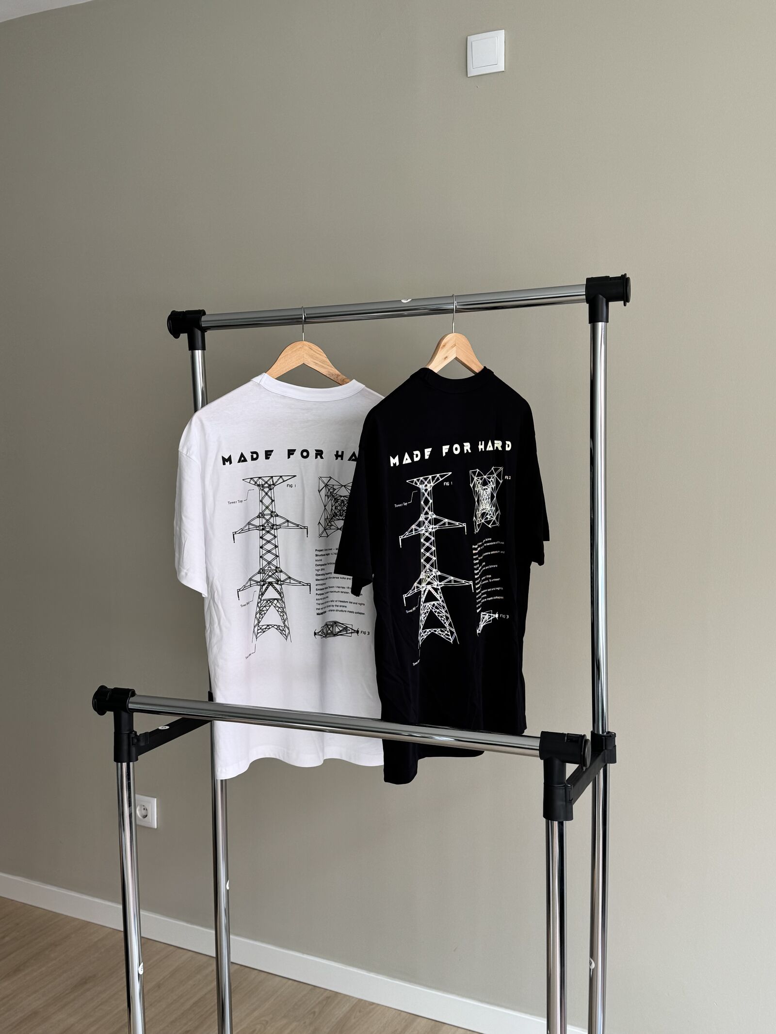 Two Made for Hard t-shirts in white and black with technical illustrations on rack