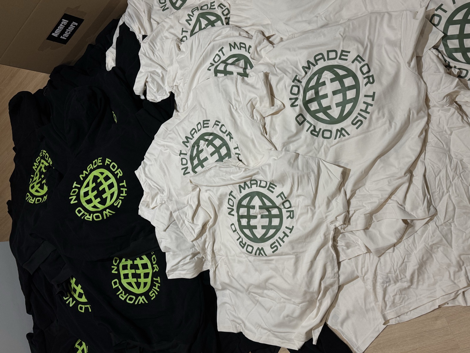Pile of printed t-shirts in black dark green and white colorways featuring globe graphic with Not Made for This World text
