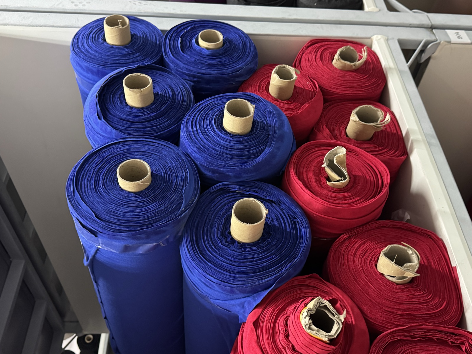 Rolls of royal blue and red knit fabric stacked on factory storage shelves