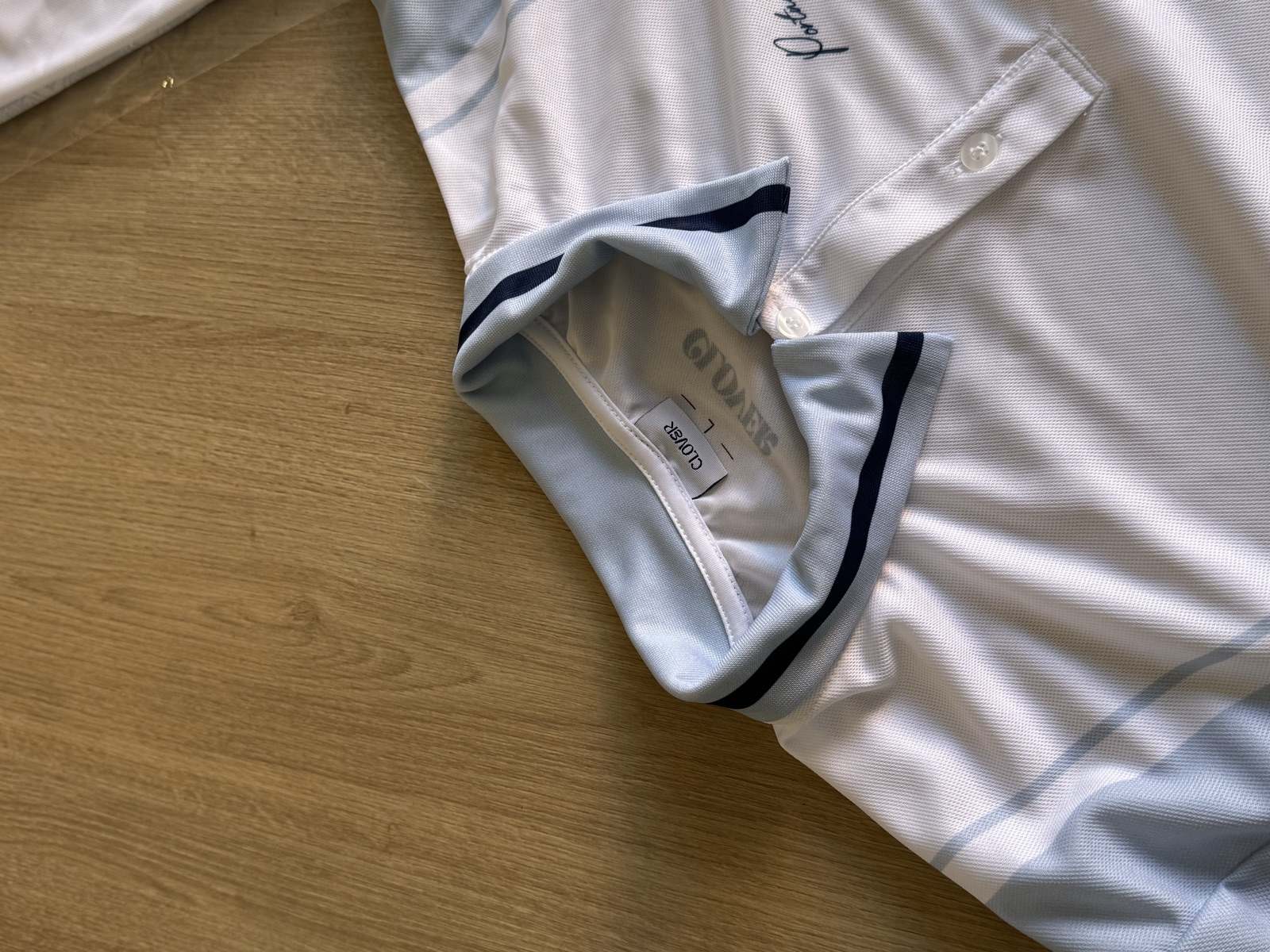 Interior detail of white sports jersey showing Clover branded neck label with navy trim and clean construction