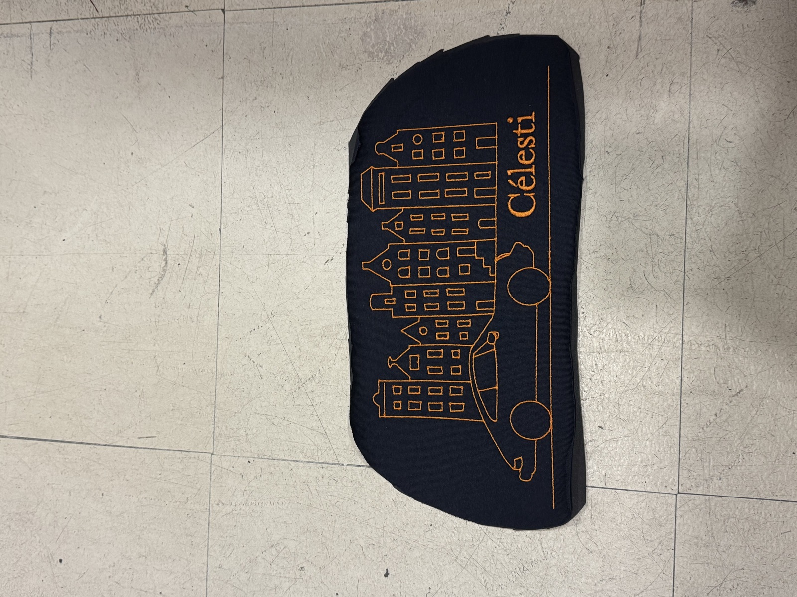 Dark navy custom-cut fabric piece with orange line illustration of cityscape and classic car branded Celesti