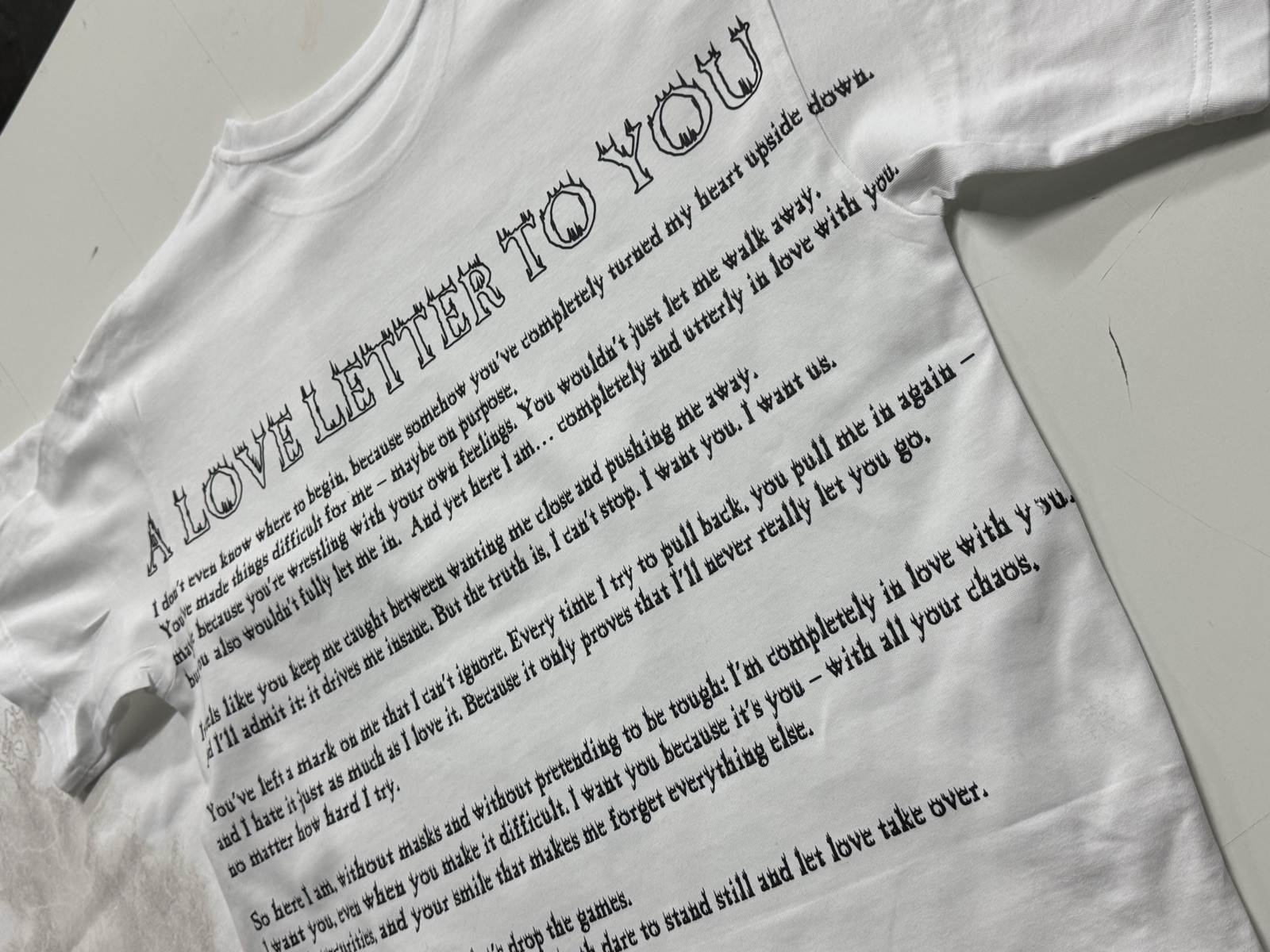 White t-shirt printed with A Love Letter to You heading followed by decorative serif typography block