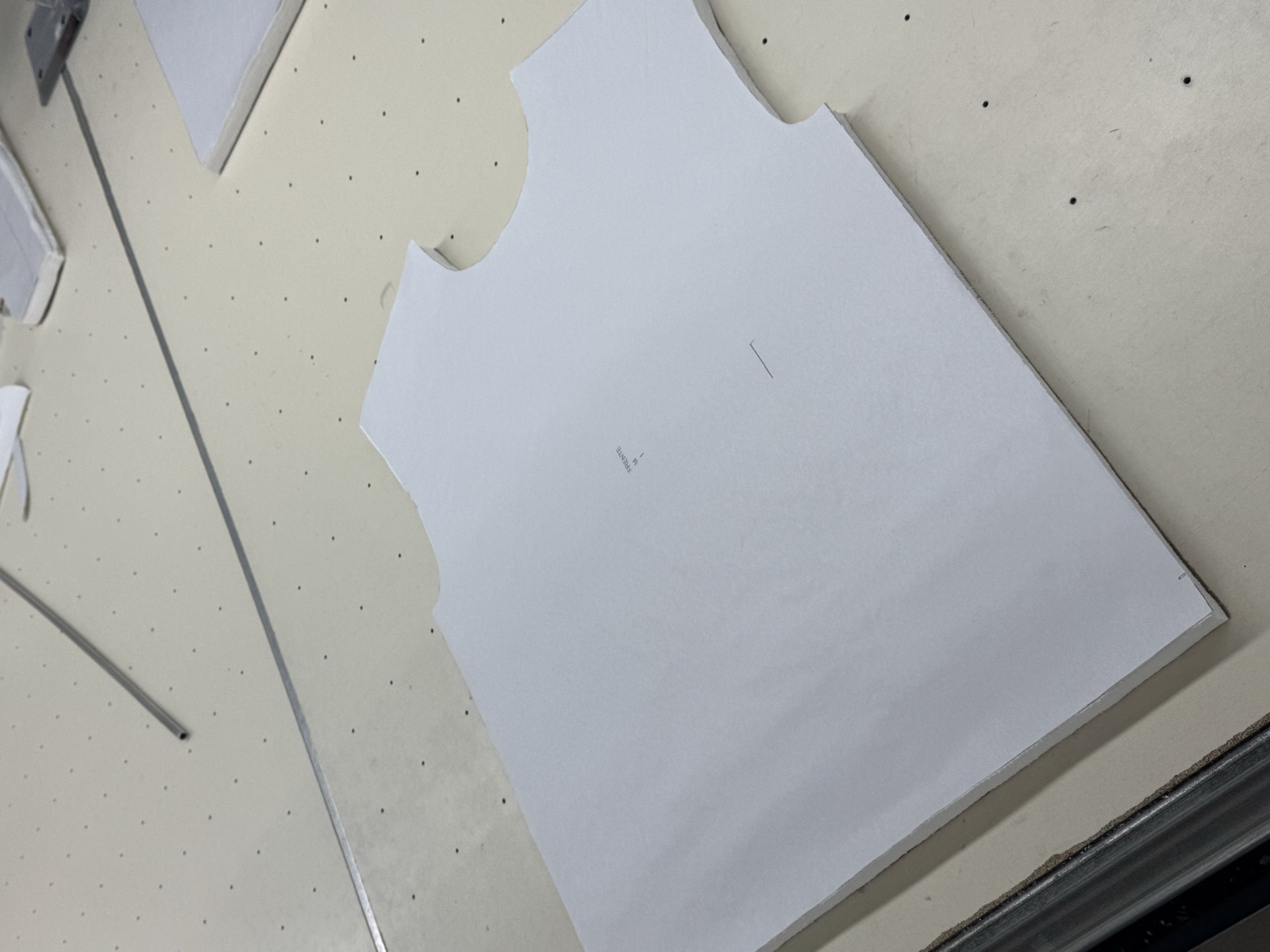 Paper pattern template for sleeveless garment body panel laid out on perforated cutting table in factory