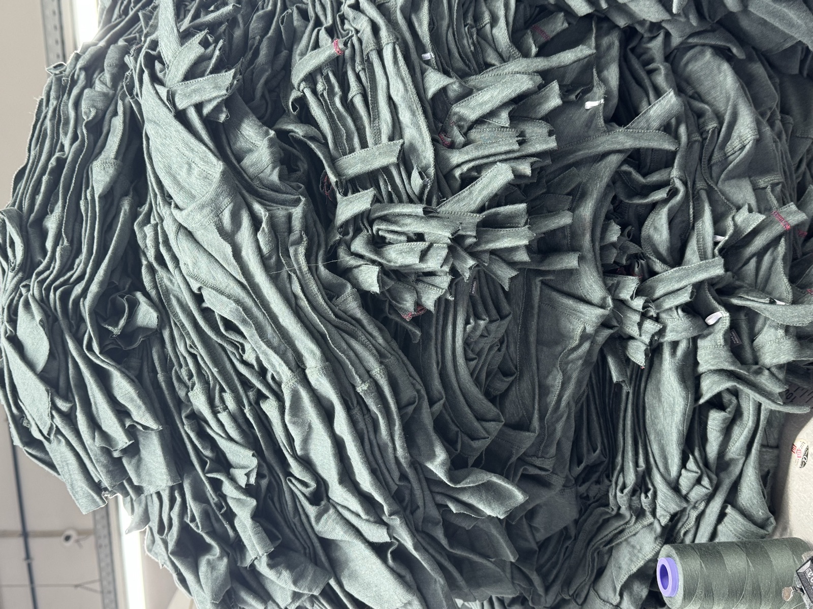 Large batch of dark green cut fabric panels stacked and bundled together ready for sewing production