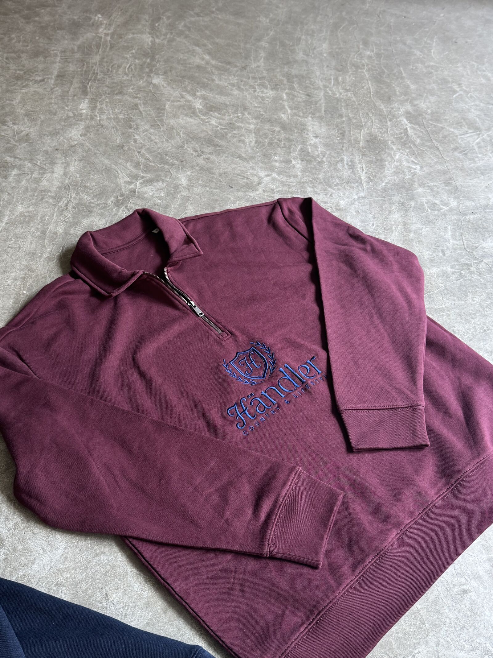 Burgundy zip-up hoodie with blue embroidered script logo and crest