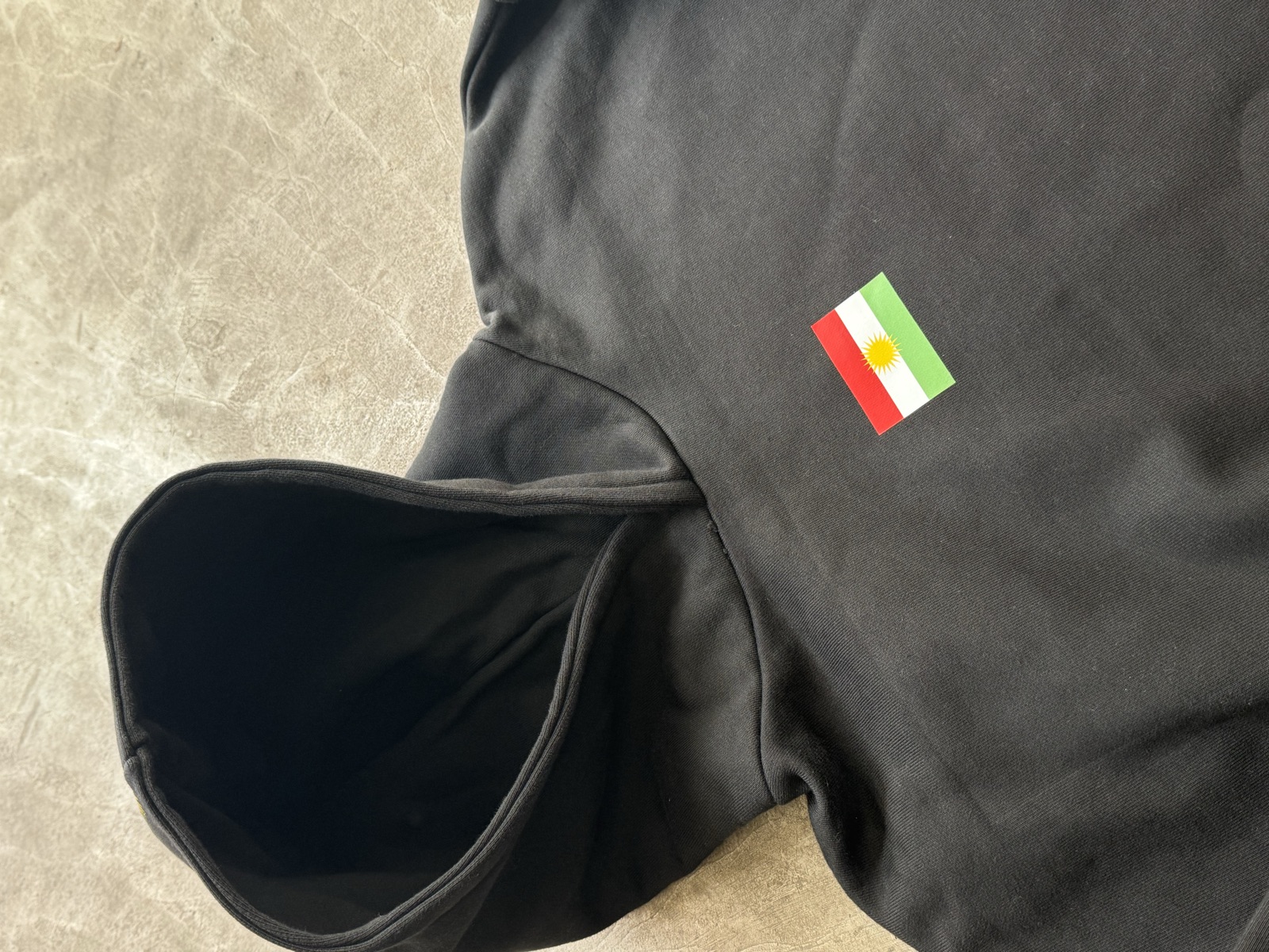 Black hooded sweatshirt laid flat showing small embroidered Italian flag patch on chest with hood folded open