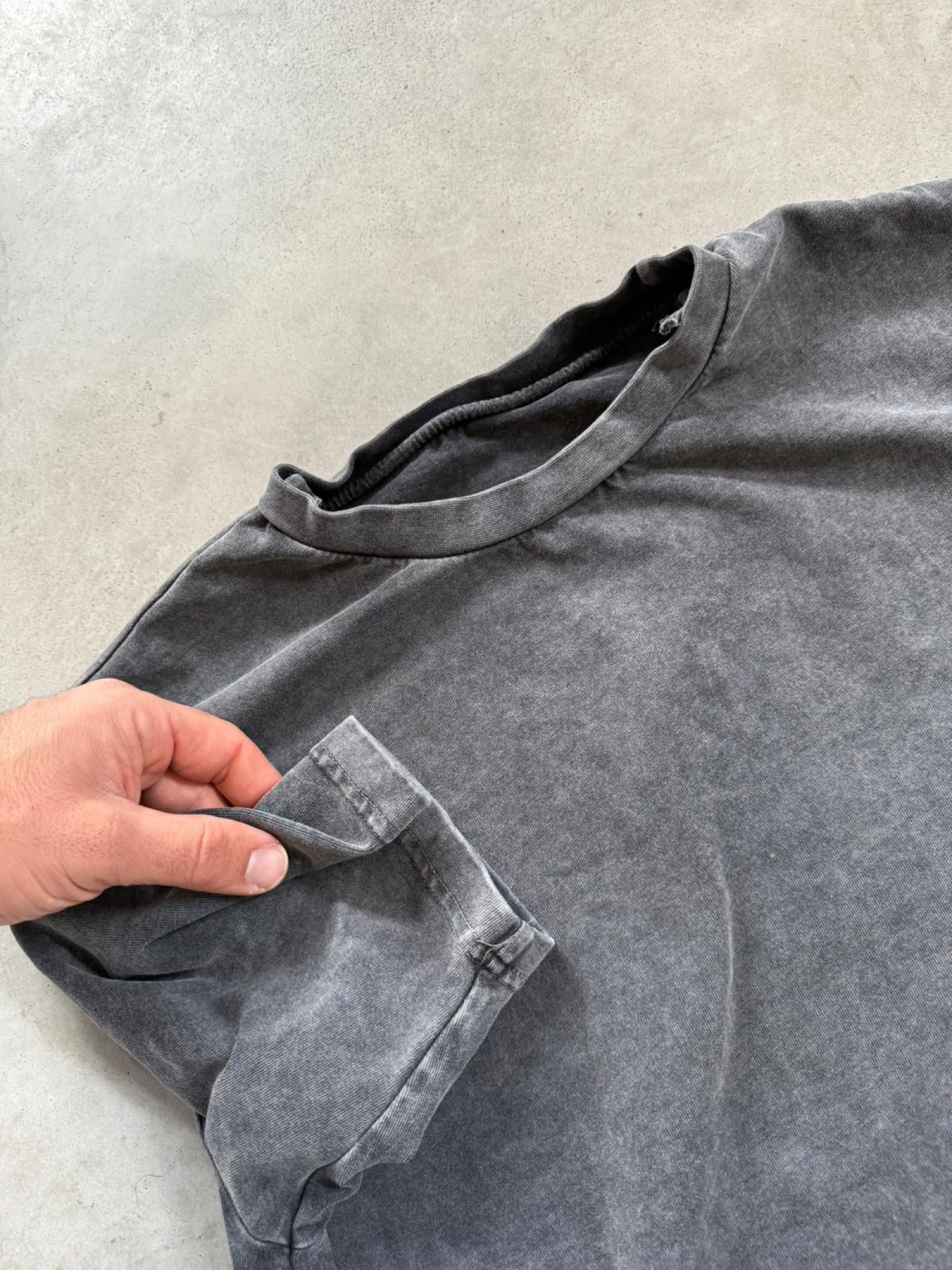 Hand inspecting charcoal stone-washed t-shirt neckline and sleeve showing vintage wash texture
