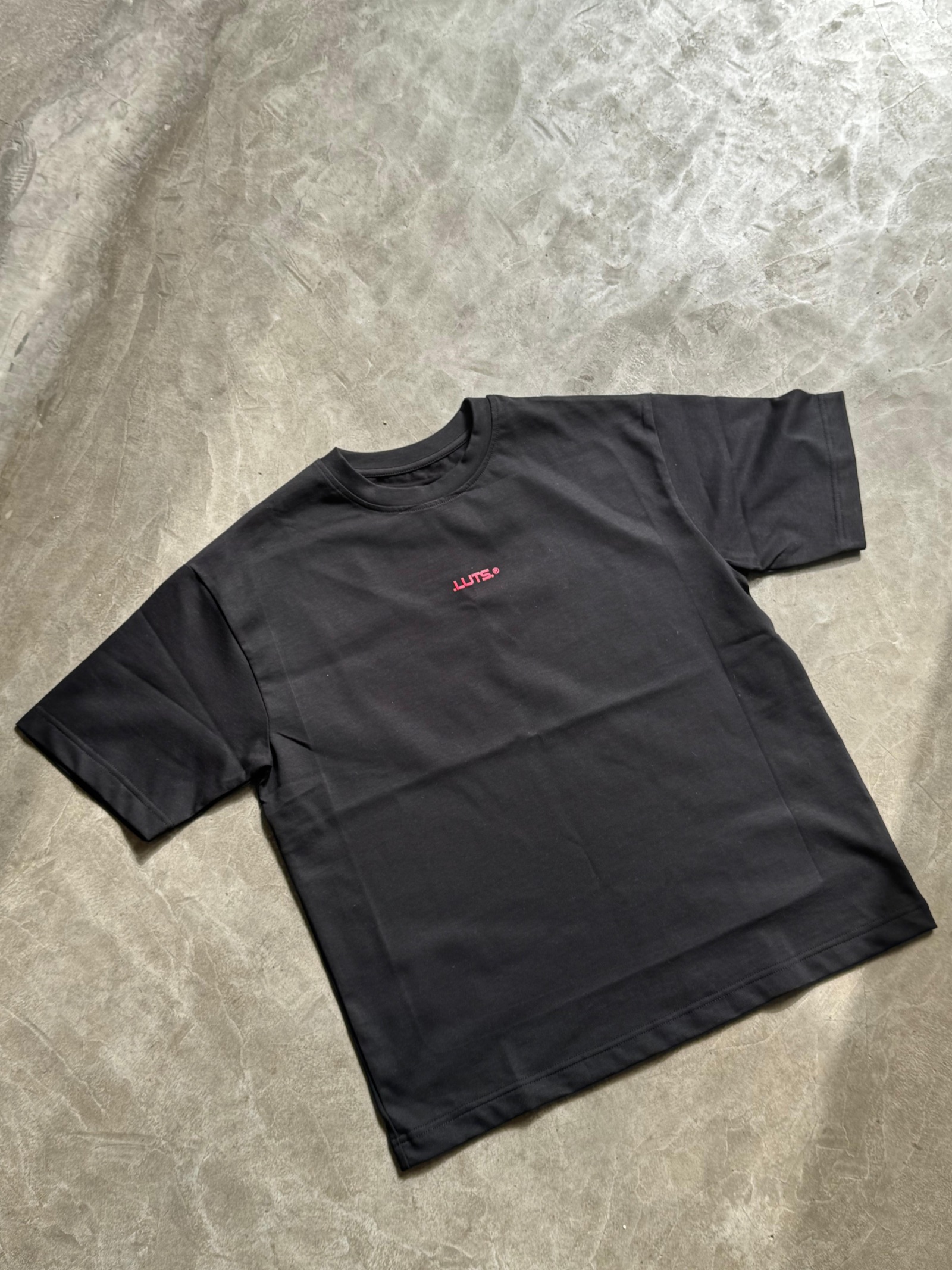 Black oversized t-shirt with small pink centre chest logo on concrete surface
